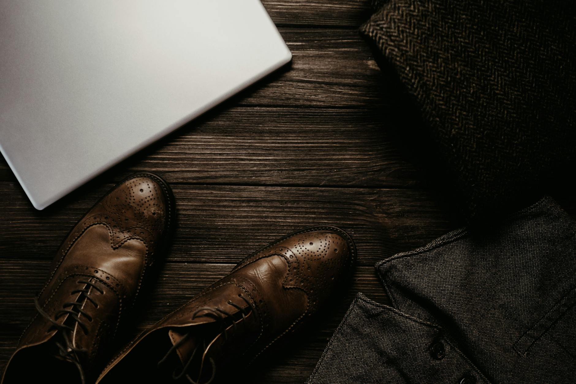 Brązowe skórzane lakierki obok laptopa i ubrań na drewnianej podłodze