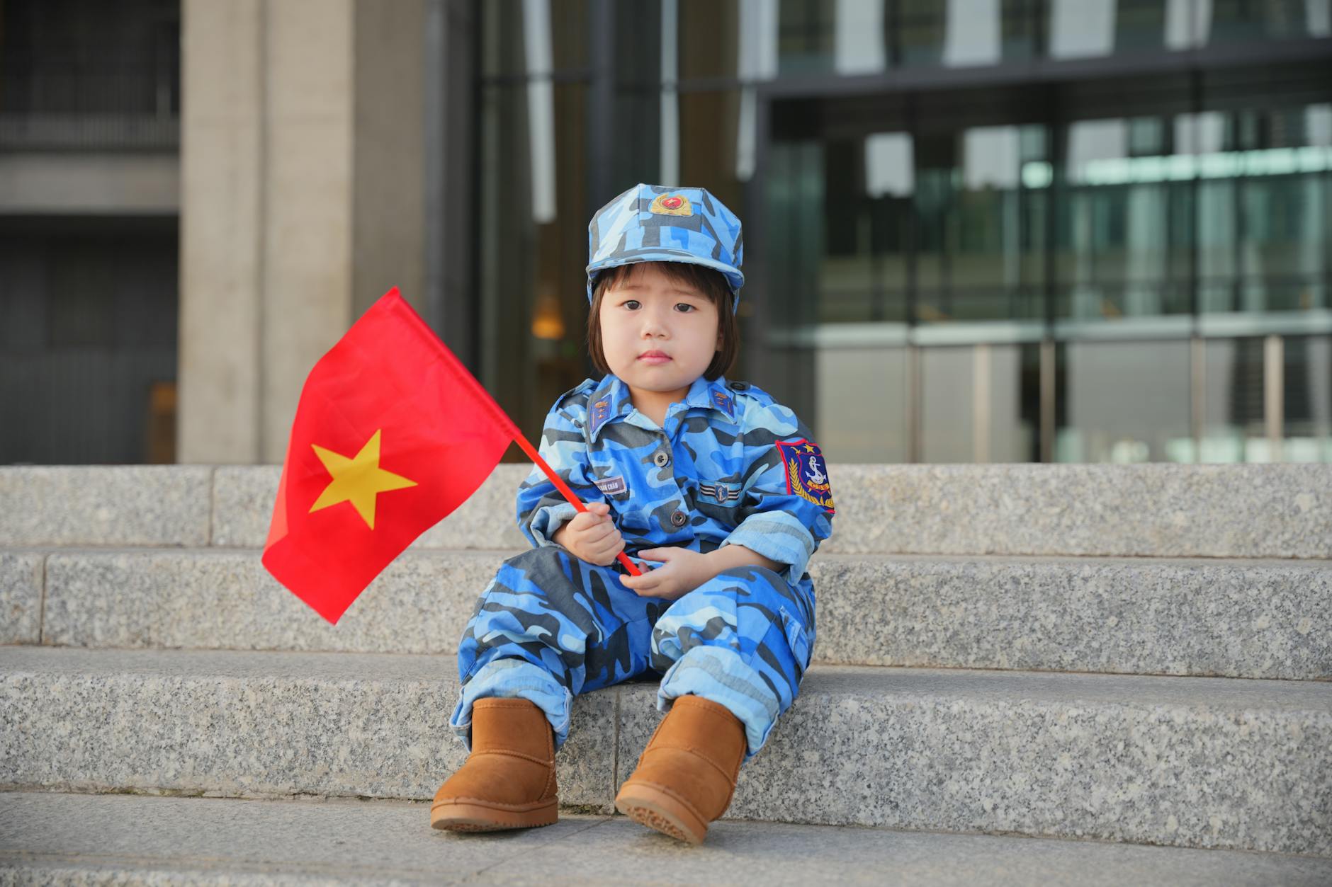Dziecko w niebieskim mundurze wojskowym siedzi na schodach z flagą Wietnamu