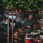 Szewc w ulicznym warsztacie otoczonym różnymi parami butów vintage