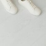 Białe damskie sneakersy na jasnej drewnianej podłodze, widok z góry