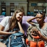 Dwie młode kobiety w lounge na lotnisku czekają na lot z plecakami