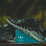 Czarne sneakersy Adidas na zewnątrz obok charakterystycznego niebieskiego pudełk
