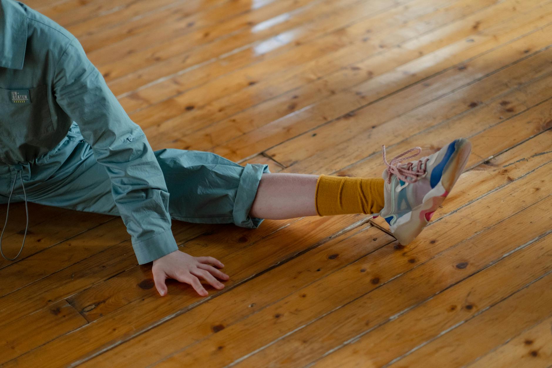Osoba rozciągająca się na drewnianej podłodze w kolorowych sneakersach