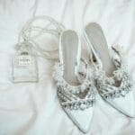 Białe szpilki z perełkami i perfumy Chanel na białej pościeli