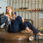 Kobieta mechanik w kombinezonie siedzi na zabytkowym aucie w warsztacie