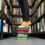 Osoba w butach stoi na kolorowych książkach między regałami w bibliotece
