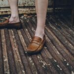 Brązowe skórzane mokasyny na stopach stojących na zardzewiałej blasze