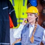 Inżynierka w kasku rozmawia przez telefon w hali przemysłowej