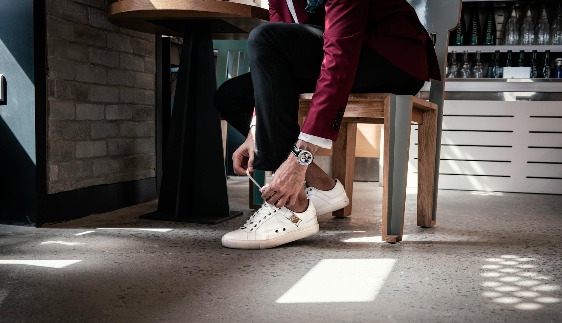 Mężczyzna w bordowej marynarce wiążący sznurówki eleganckich sneakersów