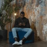 Mężczyzna w sneakersach siedzi na fotelu i korzysta ze smartfona