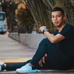 Młody mężczyzna w czarnych sneakersach i casualowym stroju siedzi na chodniku