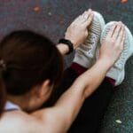 Biegaczka w sportowych butach i smartwatchu rozciąga nogi na asfalcie