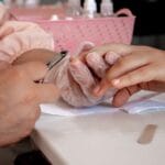 Manicure w salonie, dłonie specjalistki w rękawiczkach przy paznokciach