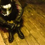 Mężczyzna w cyberpunkowym stroju z protezą ręki siedzi na drewnianej podłodze