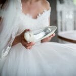 Panna młoda w białej sukni trzymająca but ślubny w dłoni