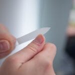 Zbliżenie dłoni piłujących paznokcie pilniczkiem w domu