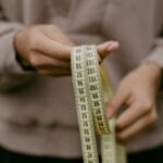 Dłonie trzymające żółtą miarkę krawiecką do mierzenia stopy